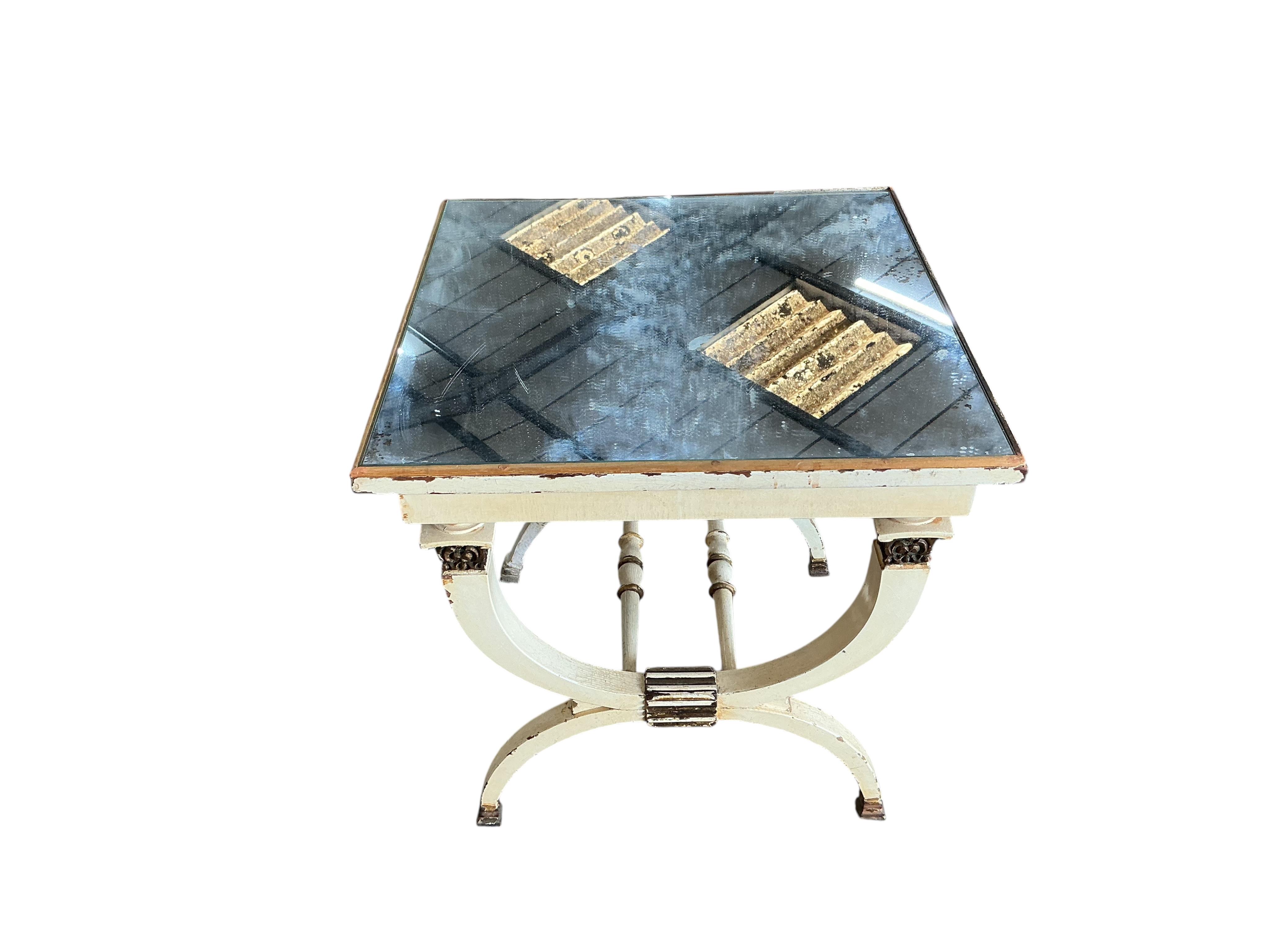 A cream, gilt and mirrored X-framed occasional table, in Empire style, width 49cm, depth 49cm, height 52cm